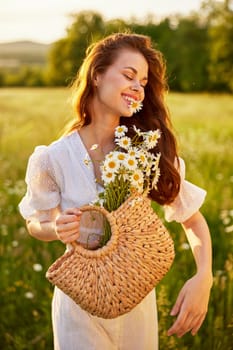 cute, happy woman with a basket of flowers in nature holds a camomile in her mouth with her eyes closed. High quality photo