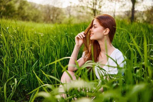 a young woman sitting resting in the tall grass straightening her hair. High quality photo