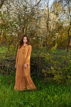 an elegant, sophisticated woman poses relaxed standing near a wicker fence at the dacha in a long orange dress. High quality photo