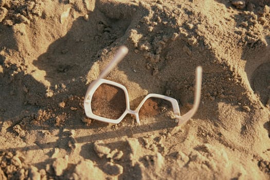 close up photo of sunglasses lying in the sand by the sea. High quality photo
