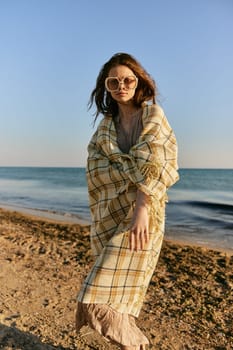 a woman wrapped in a plaid stands on the seashore in bright sunglasses. High quality photo