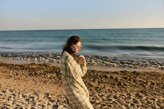 pensive woman wrapped in a blanket stands against the backdrop of the sea. High quality photo