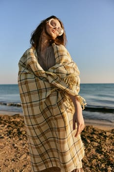 cute woman stands with a plaid during sunset on the beach. Rest, enjoyment. High quality photo