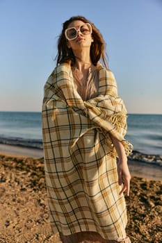 a woman wrapped in a plaid stands on the seashore in bright sunglasses. High quality photo