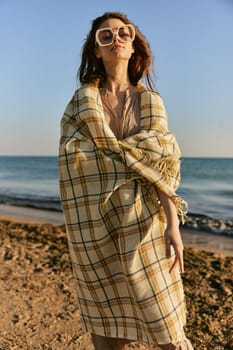 a woman wrapped in a plaid stands on the seashore in bright sunglasses. High quality photo