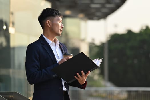 Portrait of adult businessman in formalwear standing outside building with cityscape background in early morning.