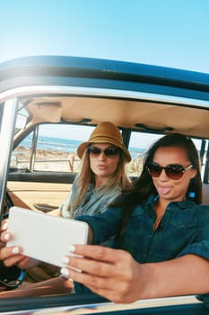 Recording road memories. two friends taking a selfie while on a road trip near the ocean