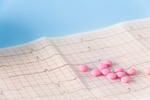 A large handful of pink pills lie on the electrocardiogram of the heart on a blue background. The concept of a healthy lifestyle and timely medical examination