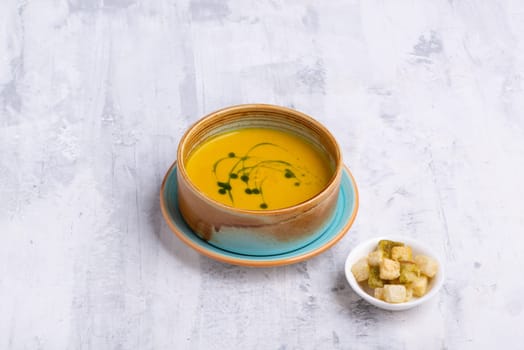 A top view of a pumpkin soup in a bowl with bread crumbs on the side on a white table