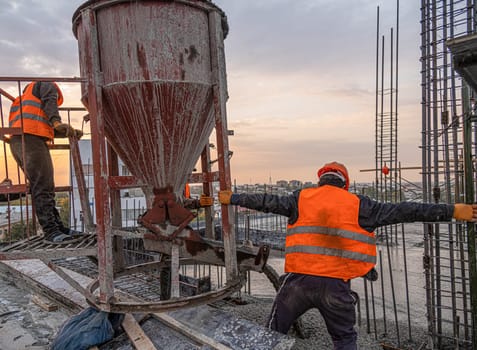 The workers on a building infrastructure roof with machinery and tools. Pouring concrete into a mold