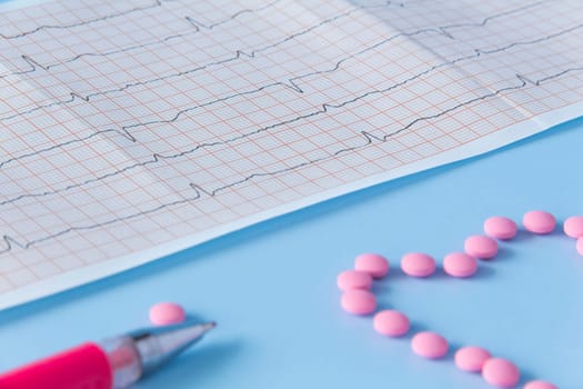 A large handful of pink pills lie in the form of a heart on an electrocardiogram, on a blue background. The concept of a healthy lifestyle and timely medical examination.