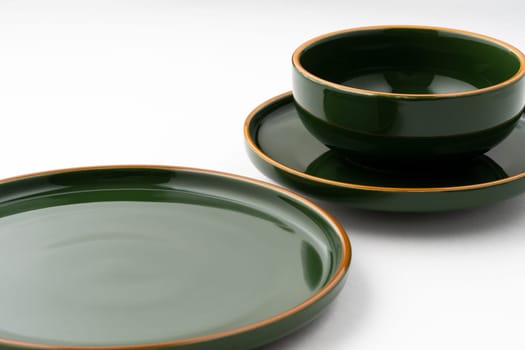 A set of dark green ceramic tableware with orange outlines on a white background