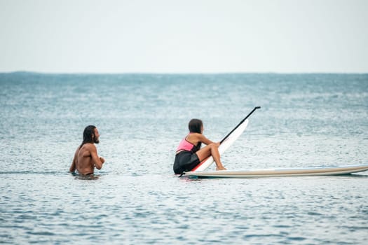 Sea woman and man on sup. Silhouette of happy young woman and man, surfing on SUP board, confident paddling through water surface. Idyllic sunset. Active lifestyle at sea or river