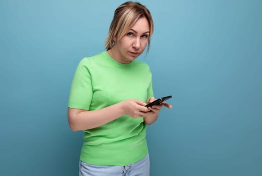attractive blond girl meditates holding a smartphone in her hand on a blue background with copy space.