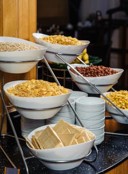 A vertical shot of a buffet table full of bowls with cornflakes, peanuts and cereal for breakfast