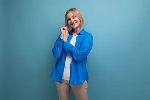 modest mature woman with blond hair in a casual shirt on a blue background with copy space.