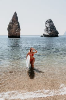 Close up shot of beautiful young caucasian woman with black hair and freckles looking at camera and smiling. Cute woman portrait in a pink bikini posing on a volcanic rock high above the sea