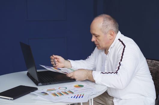 Male businessman works on laptops, studies reporting documents, charts and graphs.