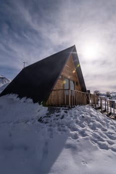 A vertical shot of a wooden cottage surrounded by snow. A recreation area in the mountains