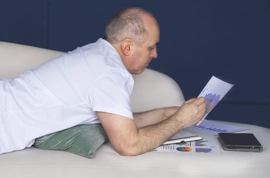 A businessman lies on a couch and looks at data trends on charts and graphs. Distant work