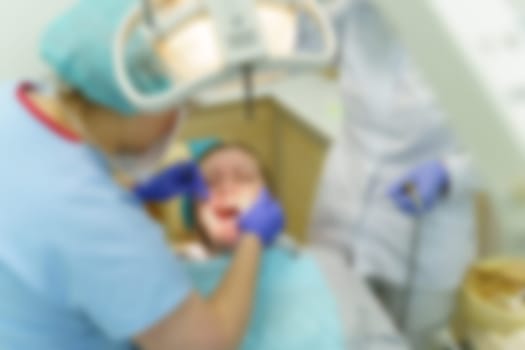 The dentist treats the teeth of the patient in the clinic. Close-up of the face, gloved hands, tools for dental treatment. Background image, blurry.