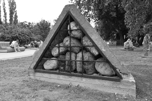 Grayscale of an art installation of stone heads behind bars in a concrete wall in Moscow, Russia