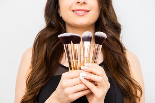 Smiling girl holding professional makeup brushes on the white background.