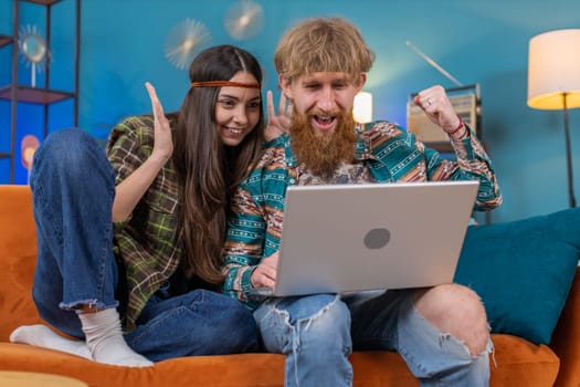 Overjoyed family marriage hippie couple man woman use laptop celebrate great big win good news lottery jackpot, lucky victory, playing game, shopping online at home. Husband and wife together on sofa