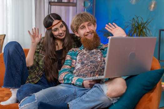 Young family marriage hippie couple man woman making video laptop webcam conference call with friends or family, enjoying pleasant conversation at home. Husband wife laughing, waving hello in room