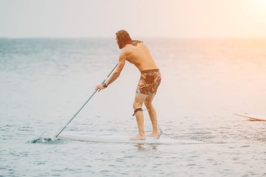 Sea woman and man on sup. Silhouette of happy young woman and man, surfing on SUP board, confident paddling through water surface. Idyllic sunset. Active lifestyle at sea or river
