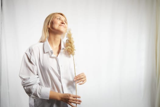 Portrait of a pretty blonde smiling woman with soft ear in hands posing on a white background. Happy girl model in white shirt in studio. The concept of softness, tenderness and dreams. Copy space