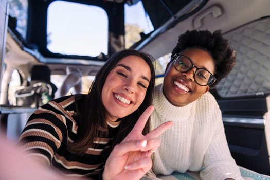 selfie photo of two happy young women having fun in a camper van, concept of weekend getaway with best friend and road trip adventure
