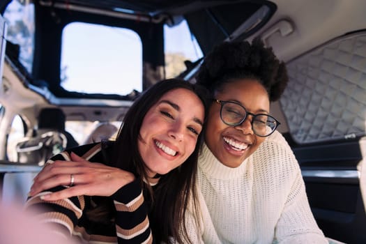 two young women having fun taking a selfie in camper van, concept of weekend getaway with best friend and road trip adventure