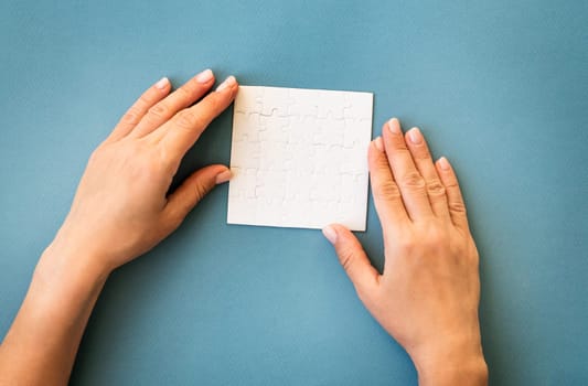 Hands with small white square puzzle on a blue background