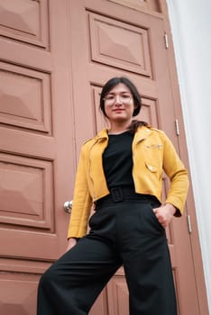 Beautiful asian woman (LGBTQ) natural makeup wear fashion yellow leather clothes with glasses posing at old town and vintage building outdoor fashion style