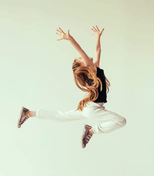 Excited young girl leaping in the air with her hands raised. Sport, training, dancing lifestyle.