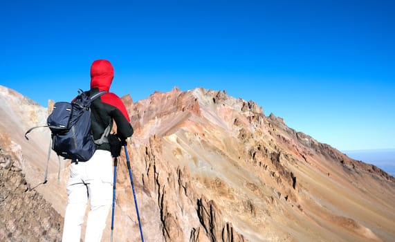 Hiker standing backwards and looking at rocky mountain peak