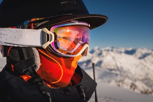 Profile of a female skier in ski goggles in the mountains. A woman in a sports ski jacket and snowboard sunglasses looks away. Sportswear and fashion for winter sports, ski resort.