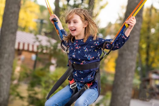 Happy little girl jupmping on trampoline ropes in adventure park in autumn