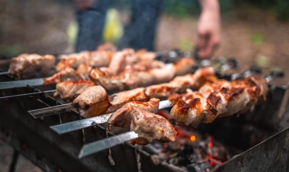 Man hand straightens the metal skewer with barbecue delicious grilled meat with smoke on brazier outdoors. Person preparing pork steaks on fired charcoals. Hot BBQ closeup