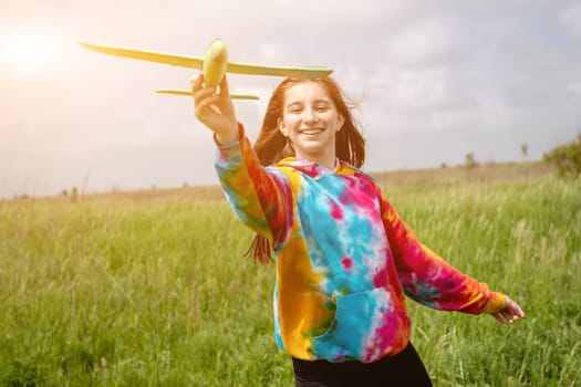 Portrait of smiling girl with toy plane outdoors in the field in sunny rays. Teenager female person launching airplane at the nature. Concept of freedom and hobby