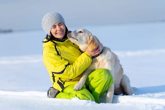 Cute young retriever dog kissing laughing woman on snowy field