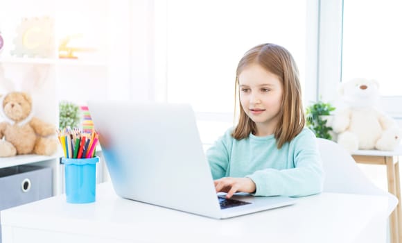 Beautiful little girl working on laptop at home