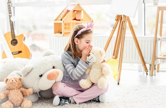 Happy little girl sharing secrets with teddy bear in light room