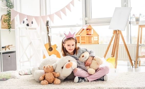 Pretty little princess hugging plush teddies in kids room