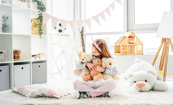 Smiling little girl hugging teddy bears sitting on floor indoors