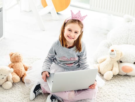 Cute little girl sitting on floor with laptop in playroom