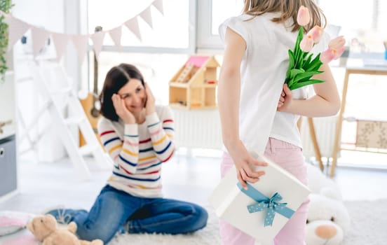 Little girl presenting beautiful gift to happy mother at home