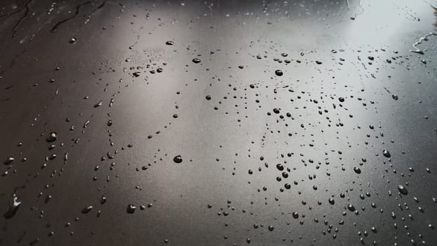 Water drops on black plastic. Surface with wet background. Abstract texture and pattern full of water. Raindrops of rain for overlaying on window with partial focus. Concept of autumn weather