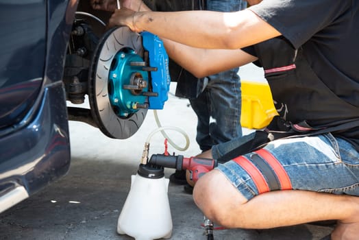 Bangkok, Thailand - March 6, 2021 : Unidentified car mechanic or serviceman disassembly and checking a disc brake and asbestos brake pads for fix and repair problem at car garage or repair shop